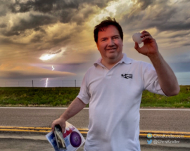 Bill shows off a big hailstone as lightning strikes behind him.